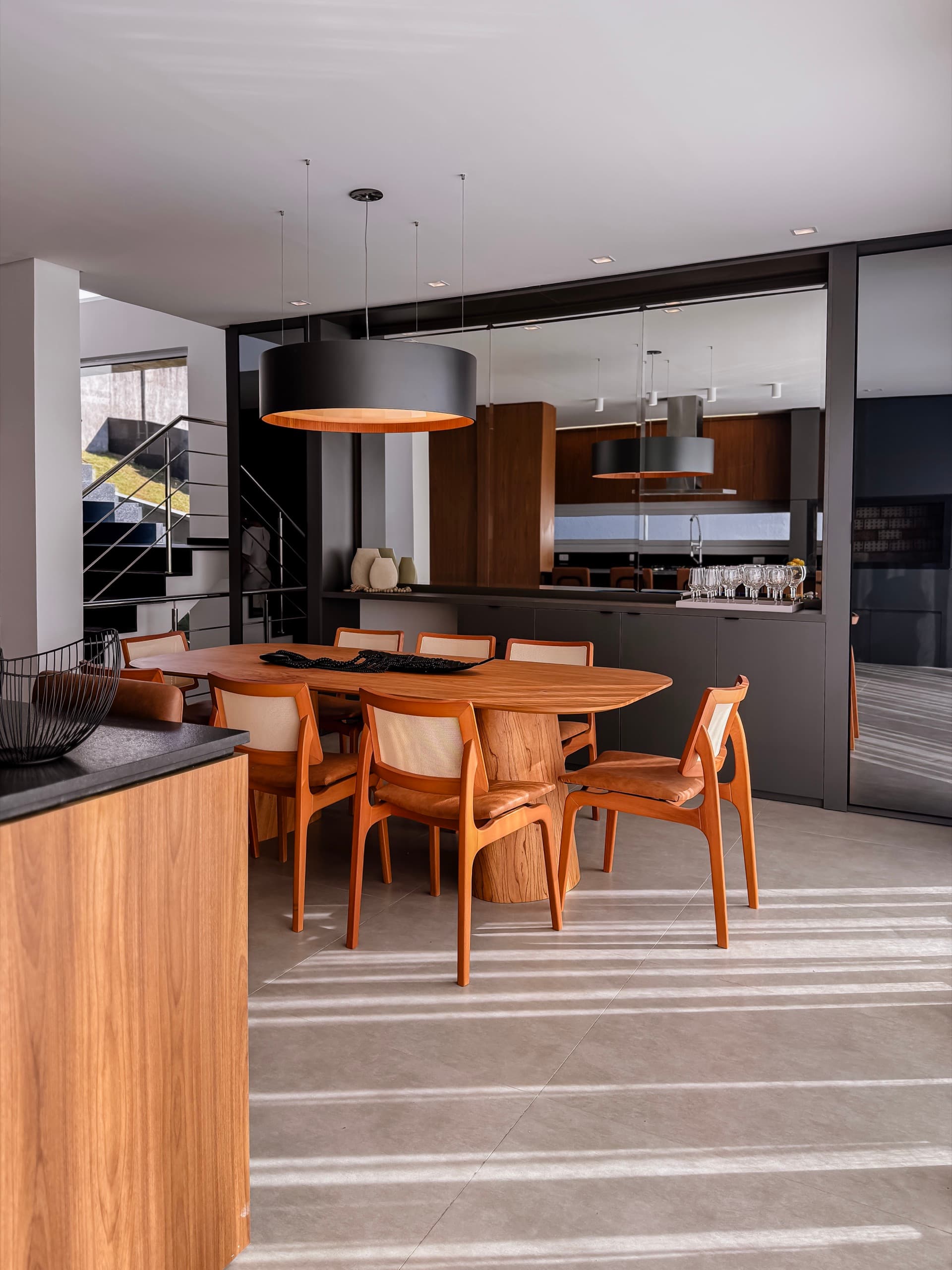 Sala de jantar com mesa orgânica em madeira e cozinha integrada ao fundo, marcenaria em nogueira e grafite