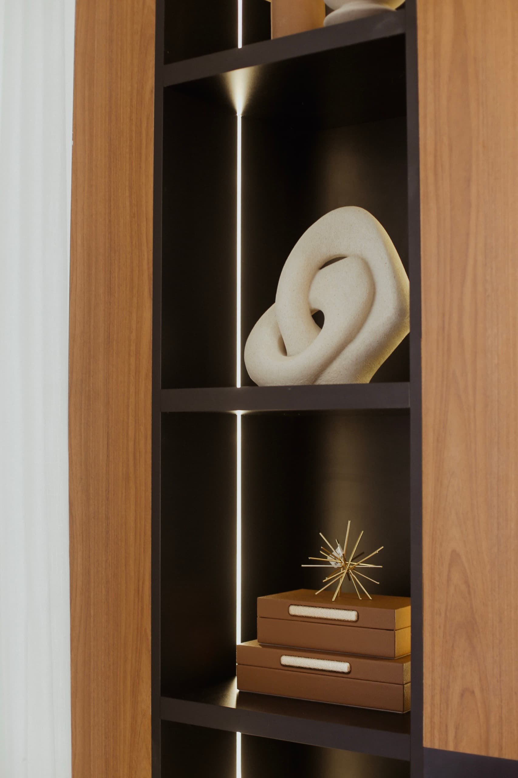 Detalhe da estante preta com iluminação vertical e objetos decorativos