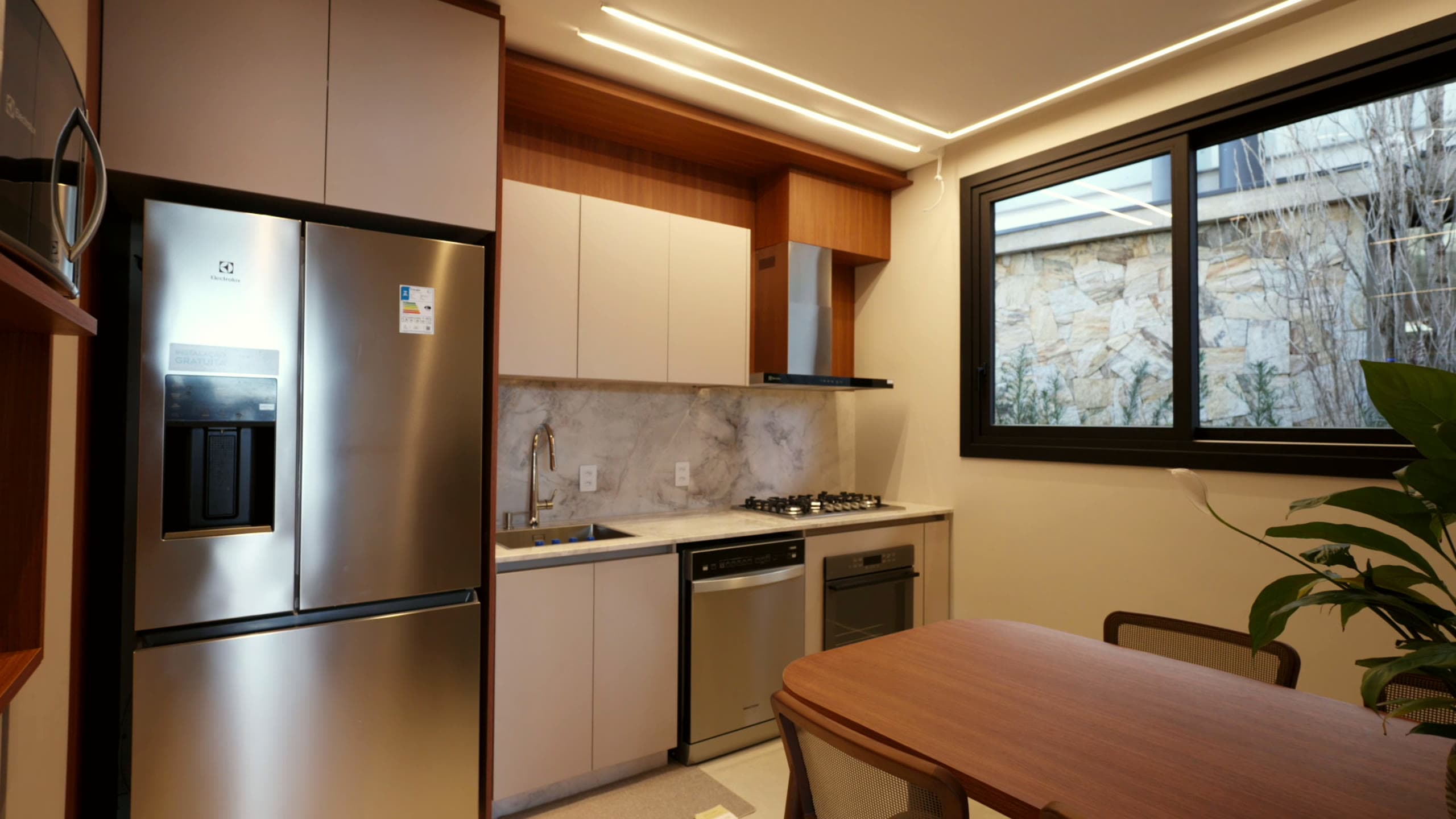 Cozinha com armários em tons neutros, eletrodomésticos embutidos e mesa de refeições