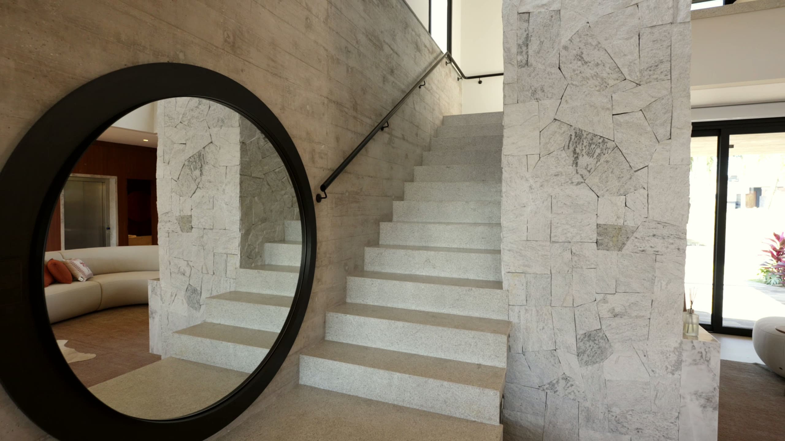 Hall de entrada com escada em pedra, espelho redondo e parede de mármore