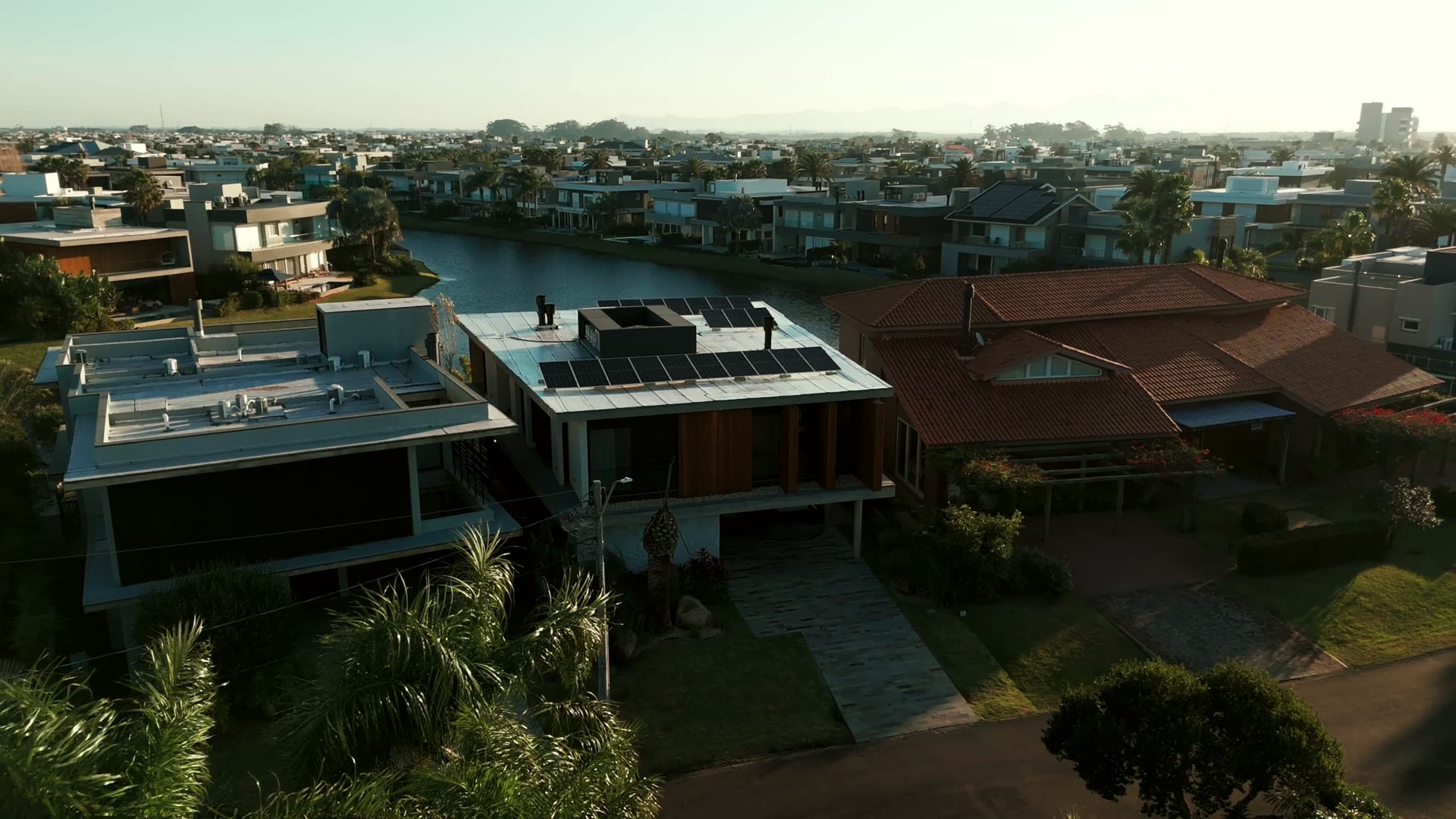 Vista aérea da fachada da casa ao entardecer, com piscina e vizinhança do condomínio