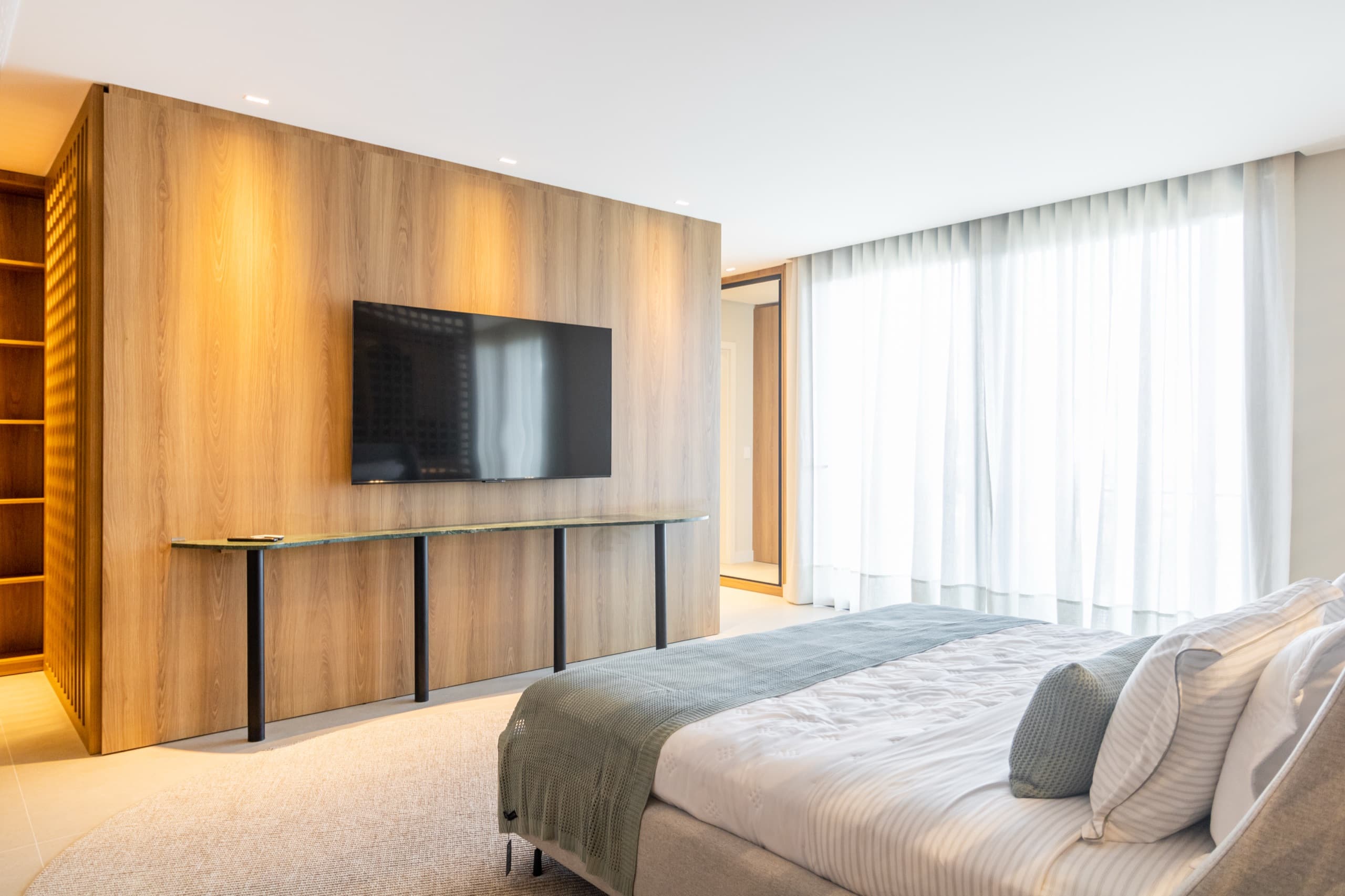 Estar da suíte master com painel de TV em madeira — vista 1