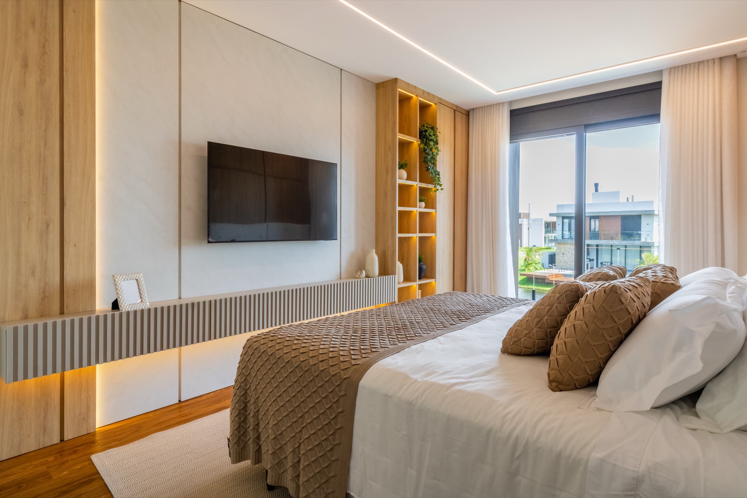 Suíte master com painel de TV, nichos iluminados e vista para o condomínio