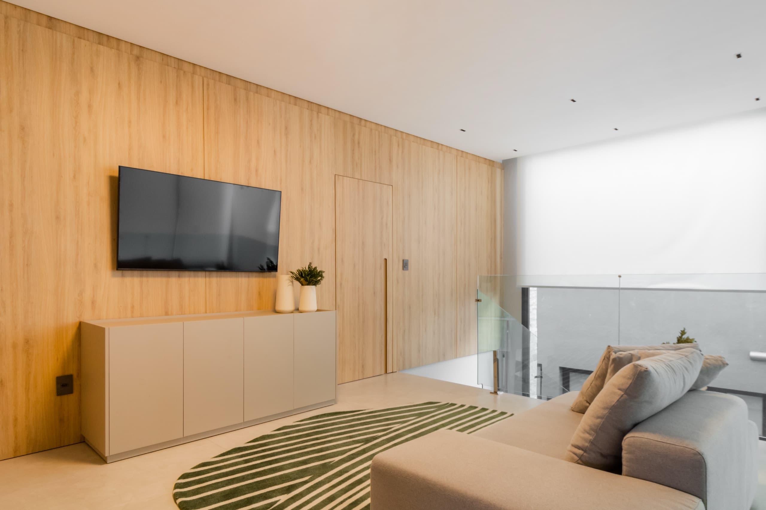 Mezanino de estar com painel de TV em madeira curva e guarda-corpo de vidro