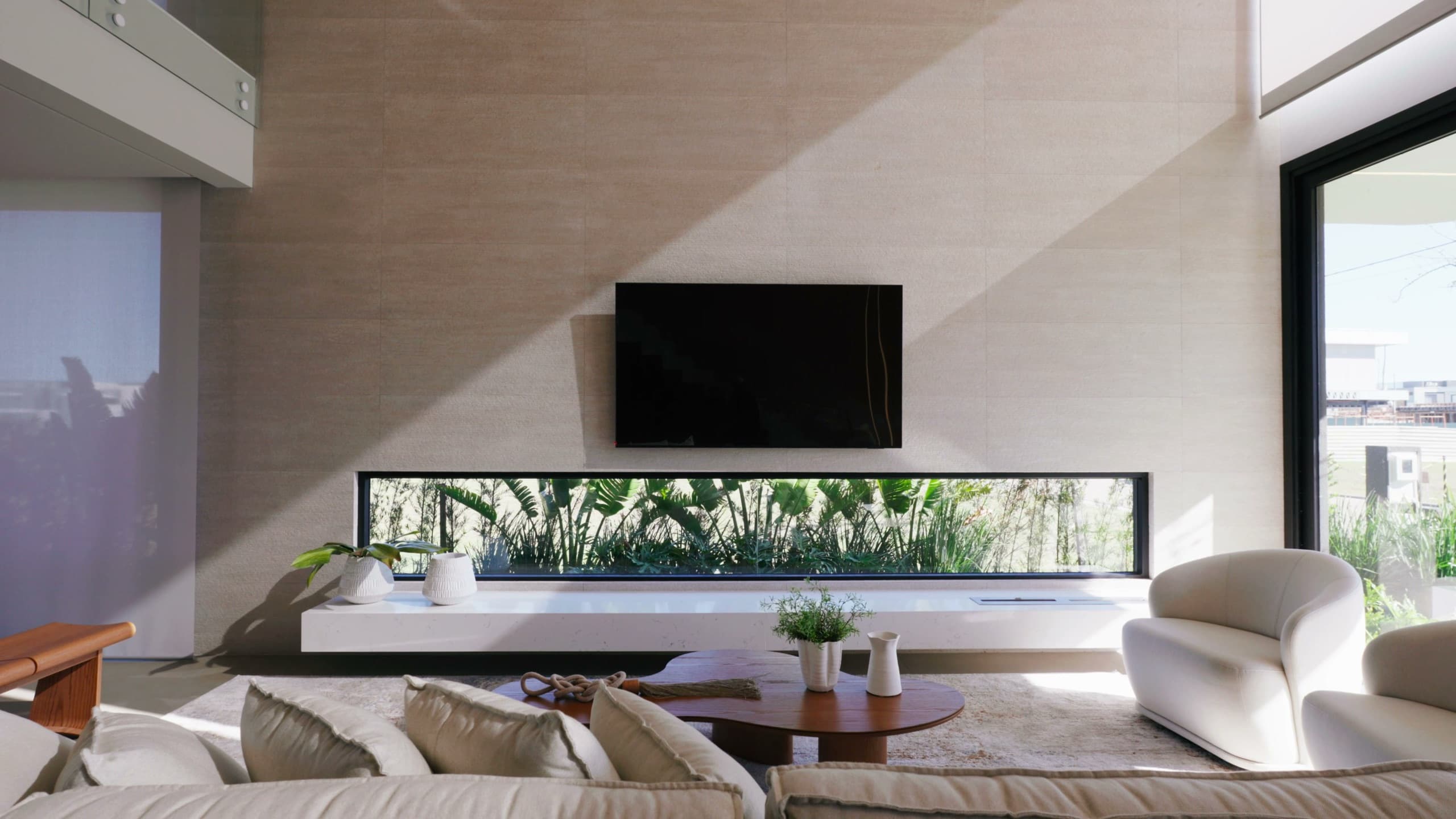 Living de pé-direito duplo com painel de TV e rasgo horizontal de vidro emoldurando o jardim tropical
