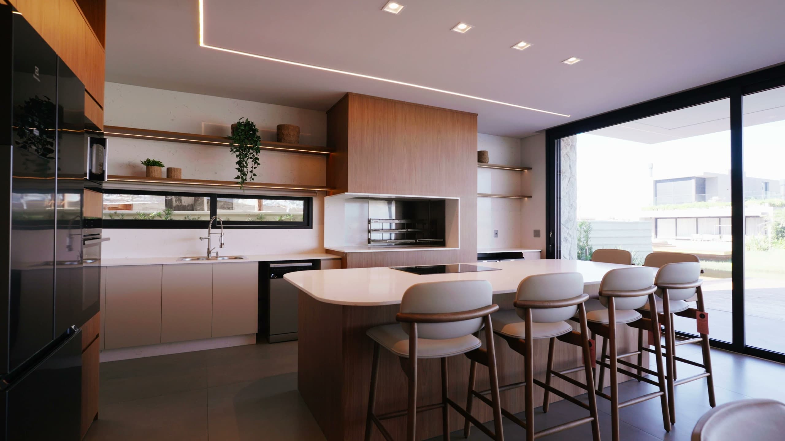 Cozinha gourmet com ilha em pedra clara, churrasqueira embutida e abertura total para o deck