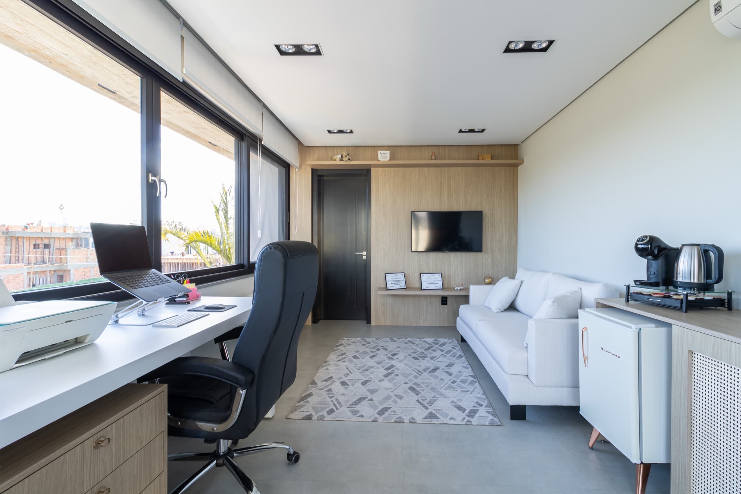 Home office com bancada de trabalho, painel de TV em madeira e sofá branco